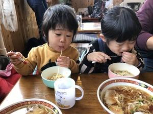小さい子ども2人が並んで熱そうなラーメンを1本ずつすすっている様子の写真