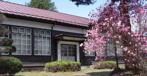 敷地内はきれいに整備され、ピンク色の桃の花が咲きく、赤い屋根とたくさんの窓がある西郷村歴史民俗資料館の外観の写真