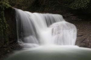 ごつい茶色の岩肌を白糸のようにきれいに流れる滝の写真